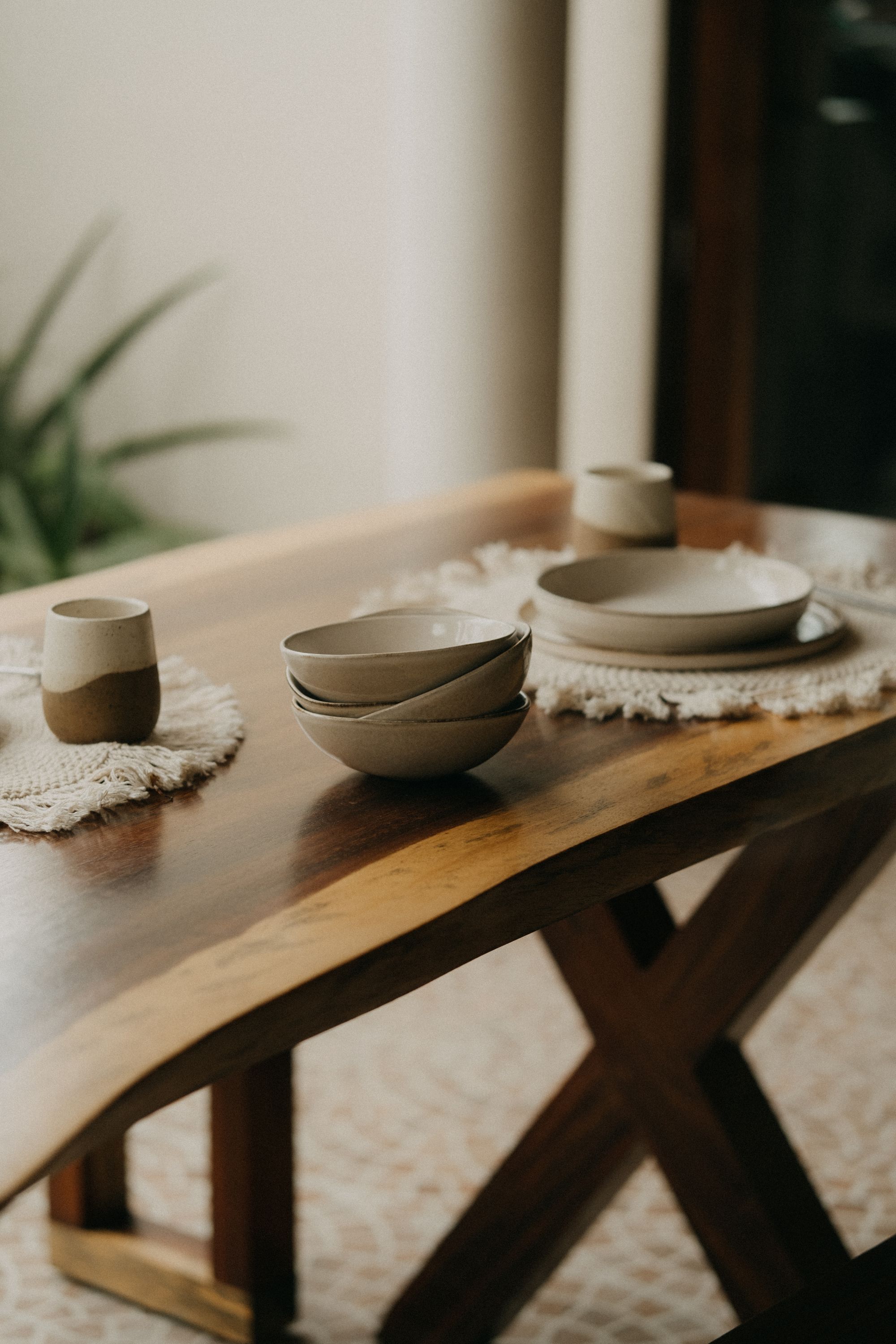 Handmade ceramic bowls, cups and plates on a warm wooden table with woven mats